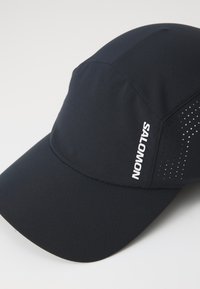 Black athletic cap made of lightweight fabric, featuring a ventilated design, a curved brim, and the "SALOMON" logo in white.