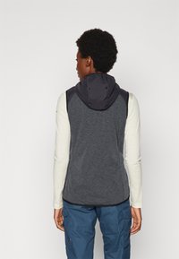 Gray vest with a black hood, featuring a textured fabric and a fitted design. Worn over a long-sleeve shirt and paired with blue pants.