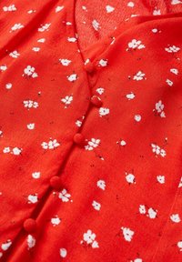 Tissu rouge à la texture douce, avec un motif floral en blanc, de petits boutons le long du centre et de délicats accents noirs.