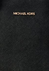 Μαύρο υφασμάτινο ύφασμα με υφή που φέρει το μεταλλικό χρυσό λογότυπο "MICHAEL KORS". Η συνολική σχεδίαση είναι κομψή και μοντέρνα με ένα διακριτικό υφαντό μοτίβο.