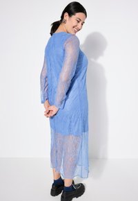 Blå spetsklänning med lång ärm, semi-transparent nedre del och scalloped fåll. Matchad med kraftiga svarta plattformsskor.