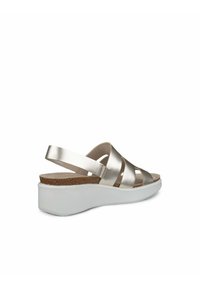 Sandały z metalicznymi złotymi paskami, korkową wkładką i białą podeszwą na koturnie. Otwarta konstrukcja z paskiem wokół kostki zapewniającym pewne trzymanie.