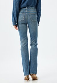 Jeans acampanados de mezclilla azul desvanecida con un diseño de cinco bolsillos, que presentan una cintura de altura media y bolsillos traseros cosidos. Llevados con tacones con patrón de piel de serpiente.