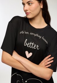 T-shirt nera a maniche corte con stampa grafica che riporta il testo "con amore, tutto diventa migliore" e un cuore rosa chiaro.