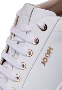 Weißer Sneaker aus glattem Leder mit goldenen Ösen, weißen Schnürsenkeln und einem erhabenen Markenlogo an der Seite.