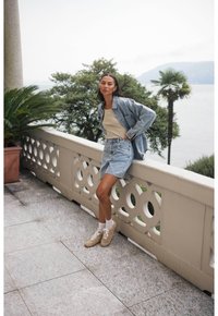 Jeansjacka, beige linne och ljusblå denimkjol. Beiga sneakers med vita strumpor. Utomhusmiljö med ett stensräcke och palmer.