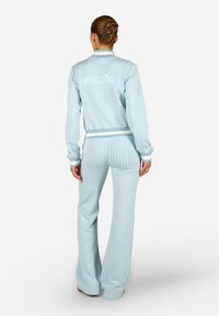 Svetlomodrá tepláková súprava z mäkkej látky s mriežkovým vzorom. Obsahuje krátku bundu s logom a rozšírené nohavice s kontrastnými manžetami.