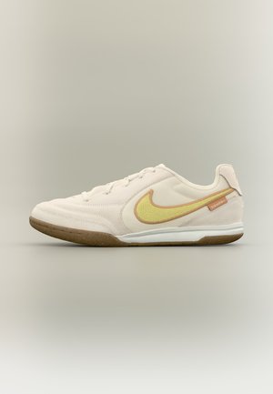 Beež Nike’i sisesneaker kollase swooshi, kummist tallaga, valge vahetalla ja ""TIEMPO"" sildiga kannakohal neutraalsel taustal.