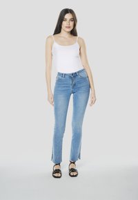 Blauwe denim hoge taille wijde spijkerbroek met zijsplitten, gecombineerd met een wit spaghetti-band topje en zwarte sandalen. Glad textuur en een aansluitend ontwerp.