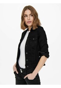 Veste en denim noir avec col, fermeture à boutons à l'avant et deux poches poitrine. Associée à une chemise blanche et un pantalon noir. Tissu texturé.
