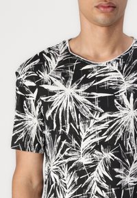 Sort t-shirt med korte ærmer, der har et hvidt abstrakt palmebladtryk, rund halsudskæring og blød struktur.