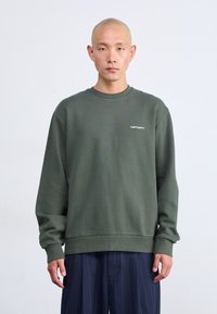 Sudadera verde hecha de tejido suave, con mangas largas, cuello redondo y un pequeño logo blanco en el pecho. Acabado texturizado.