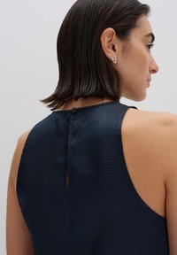 Navyblauwe mouwloze top van een gestructureerde stof, met een knoopsluiting aan de achterkant en een subtiel sleutelgatdetail.