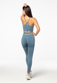 Plavi sportski crop top i uske tajice od teksturiranog materijala, s logom na pojasu i sportskim dizajnom na leđima.