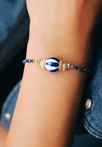 Bracelet perlé bleu et blanc avec des accents dorés. Comprend une perle centrale rayée, des petites perles bleues en alternance et du matériel doré.