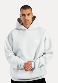 Jasnoszara bluza z kapturem z dużą kieszenią z przodu, luźny krój, ściągacze przy rękawach oraz sznurkiem do regulacji kaptura. Posiada białe logo na klatce piersiowej.