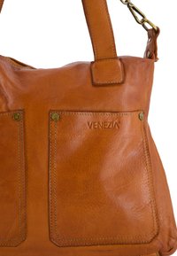 Sac à main en cuir marron avec deux poches avant, logo embossé et poignées durables. Texture lisse avec des détails de couture visibles.