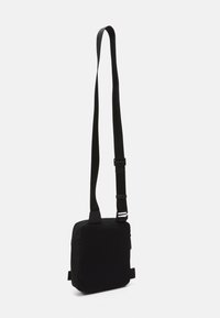 Borsa a tracolla nera con un frontale texturizzato, retro liscio, tracolla regolabile e chiusura con zip. Forma quadrata compatta progettata per l'uso quotidiano.