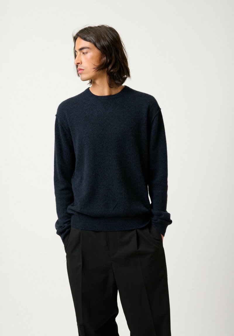 Pull bleu marine en matériau doux avec de longues manches, finitions côtelées aux poignets et à l'ourlet. Associe à un pantalon noir ample.