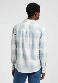 Camisa de manga larga a cuadros azul claro y blanca con cuello abotonado, dobladillo redondeado y botones en los puños, hecha de una suave tela texturizada.