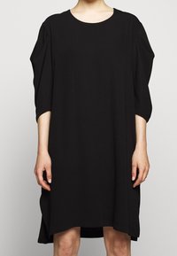 Svart klänning med rund halsringning, trekvartslånga ärmar och en löst sittande silhuett. Tillverkad av mjukt, lätt tyg. Sidofickor finns.