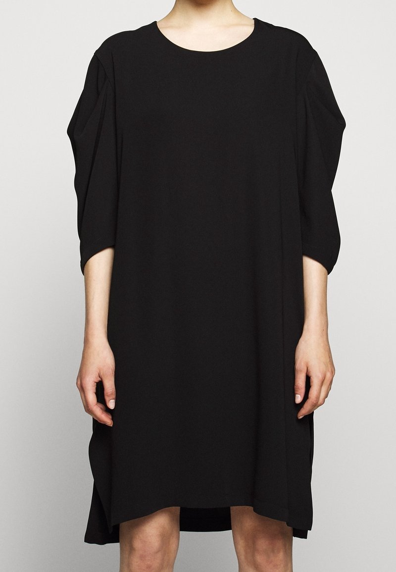 Svart klänning med rund halsringning, trekvartslånga ärmar och en löst sittande silhuett. Tillverkad av mjukt, lätt tyg. Sidofickor finns.