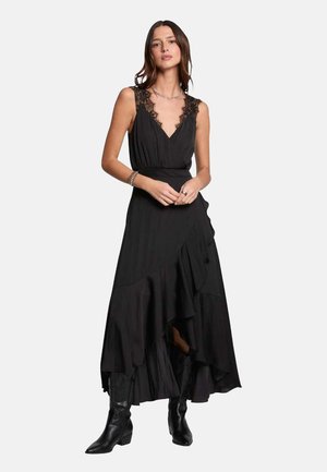 Robe maxi noire avec des détails en dentelle au niveau du col, un ourlet à couches fluide et une texture subtile, associée à des bottines noires.