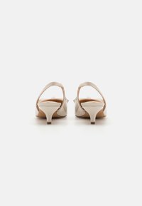 Beige patent leather heels with a low, slim heel. Open back and narrow ankle strap. Smooth texture and rounded toe design.