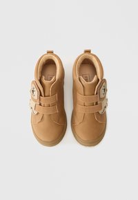 Brūni velcro apavi ar mīkstu, zamšveida tekstūru. Iespējo lauvu sejas plāksteri un izturīgu gumijas zoli. Minimālistisks dizains ar noapaļotu pirkstu daļu.