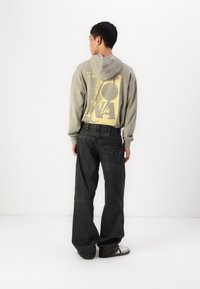 Grå hettegenser med gul grafisk design på baksiden, kombinert med mørke, vide jeans med flere lommer og en teksturert stoff.