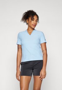 Polo shirt bleu clair à manches courtes avec un col en V, texturé de petits points en relief, associé à un short de sport noir.