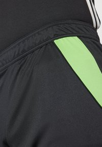 Sorte treningsshorts laget av glatt materiale med en grønn sidepanel. Midjebåndet er elastisk med søm detaljer langs kantene.