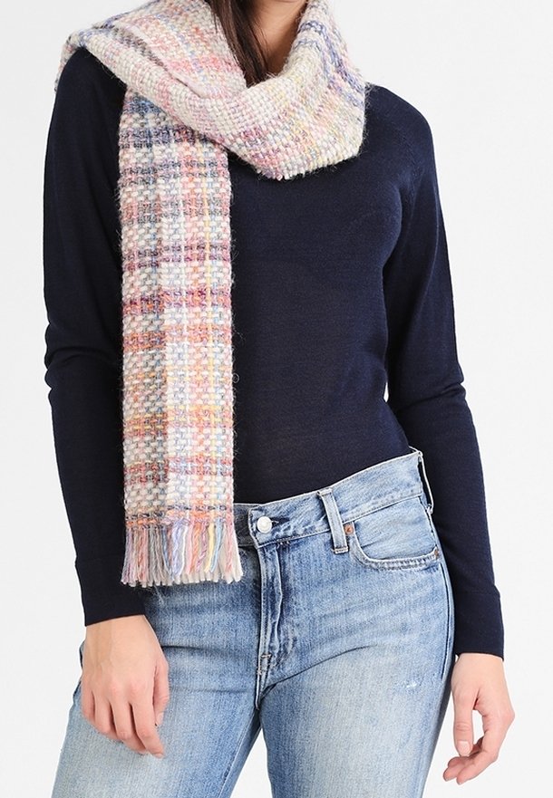 Écharpe en plaid tricotée aux couleurs pastel douces avec des accents à franges, portée sur un haut bleu marine et associée à un jean bleu clair.