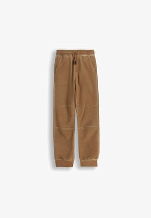 Brązowe dresowe spodnie z weluru z elastycznym pasem, sznurkiem, bocznymi kieszeniami, szwami na kolanach i prążkowanymi mankietami na kostkach na białym tle.