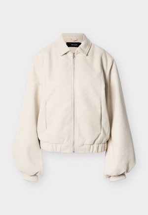 Ζακέτα με φερμουάρ σε κρεμ απόχρωση, με γιακά πουκάμισου, μακριά φουσκωτά μανίκια και ελαστική μέση, σε απλό φόντο.