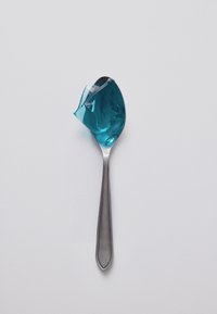 Un cucchiaio d'argento che tiene una cucchiaiata di gelatina blu traslucida su uno sfondo bianco semplice.