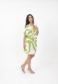 Kurzärmliges Kleid in Weiß mit kräftigen grünen abstrakten Mustern, mit V-Ausschnitt und tief sitzender Taille, aus leichtem Stoff gefertigt.
