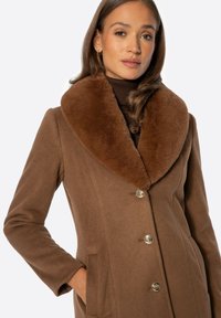 Brązowy wełniany płaszcz z dużym sztucznym futrzanym kołnierzem, guzikami w złotym odcieniu i bocznymi kieszeniami. Gładka tekstura z dopasowanym krojem.