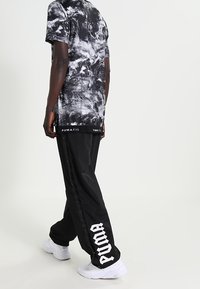 Svart och vit grafisk t-shirt med ett snurrande mönster, i kombination med svarta träningsbyxor med en vit "PUMA"-logotyp längs sidan.