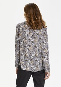 Chemise à manches longues en tissu léger avec un motif floral aux tons bleus, bruns et dorés, ourlet arrondi et poignets à boutons.