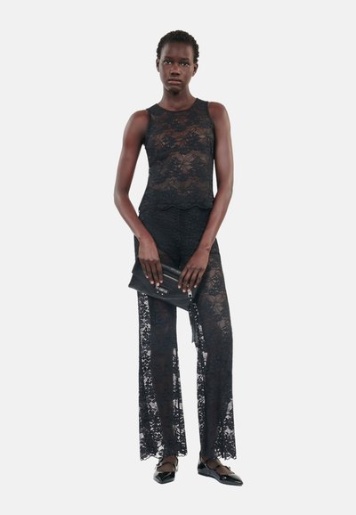 Svart blonde to-delt antrekk med ermeløs topp og vide bukser. Teksturert stoff med scalloped kanter. Kombinert med en svart clutch.