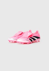 Botas de futebol cor-de-rosa com detalhes em preto, apresentando um design elegante, parte superior texturizada e uma marca em destaque na língua e no lado.