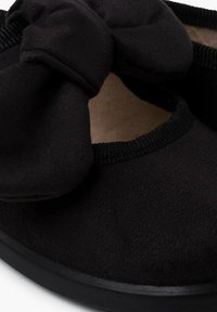 Des chaussures en tissu noir avec un détail en nœud, en matériau doux, de forme ronde, avec une garniture élastiquée et une semelle noire solide.