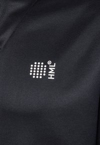 Gros plan sur un tissu noir avec le logo blanc HML composé d'un cercle de points et d'un texte vertical sur une surface textile texturée.