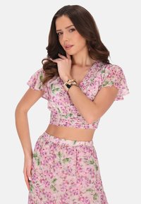 Blumen-Crop-Top und Rock-Set in hellrosa mit grünen und lilanen Blumenmustern. Leichter Stoff mit kurzen, schwingenden Ärmeln und gerafftem Bund.