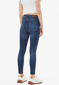 Smal jeans i mörkblå denim med hög midja, bakfickor och en slät yta, i kombination med vita sportskor.