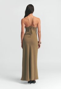 Mouwloze olijfgroene maxi-jurk met een strikdetail aan de achterkant, gemaakt van zachte stof. Heeft een strakke pasvorm en een subtiele glans.