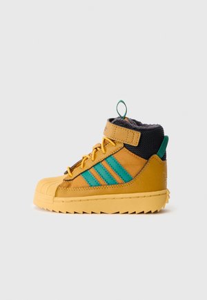 Gul højtop sneaker med grønne striber, sort polstret krave, gule snørebånd og tyk robust sål, vist fra siden på en ensfarvet baggrund.