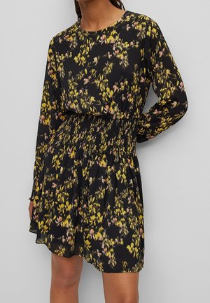 Robe noire à manches longues, ornée de motifs floraux jaunes et roses, taille smockée et jupe fluide. Texture de tissu douce.