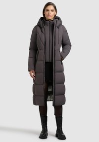 Pitkä, toppatakki tummanharmaana, jossa on huppu. Sisältää vetoketjusuljennan, sivutaskut ja hieman kiiltävän pinnan.